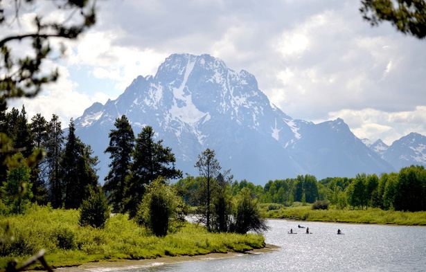 Snow-capped mountain reflected above a river with paddlers